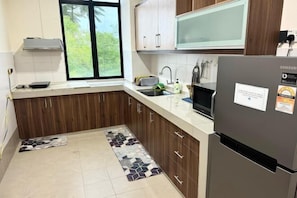 Eine moderne Küche mit Holzausbau, einem Edelstahlkühlschrank, einer Mikrowelle und einem Fenster mit Blick ins Grüne.