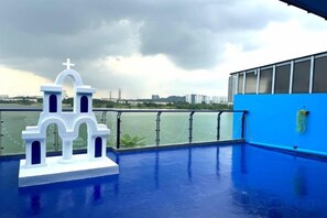 A rooftop pool with a white church-like structure, a blue wall, and a view of a cityscape. - Santorini 3000sqft Townvilla, rooftop BBQ, 5BR, 13pax (Puchong)