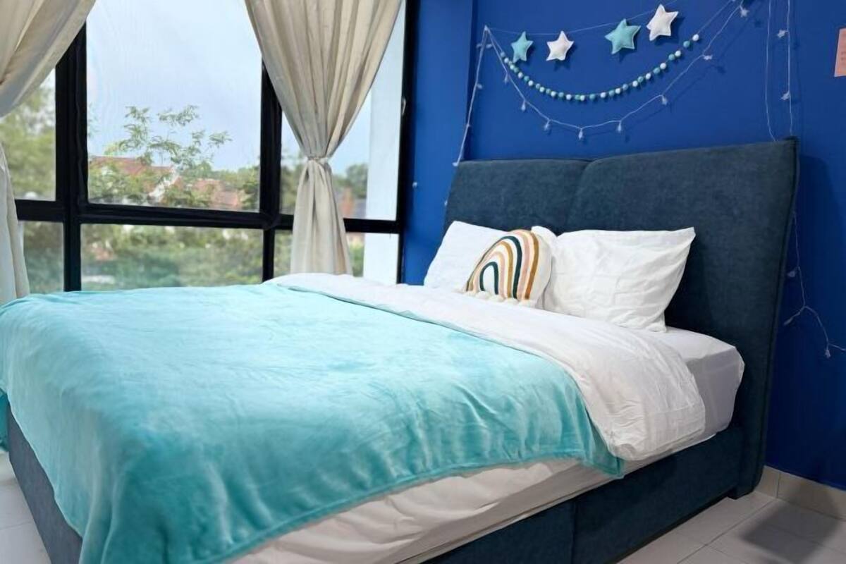 Un lit recouvert d’une couvre-lit turquoise, agrémenté d’oreillers blancs et doté d’une tête de lit bleue, dans une pièce avec une grande fenêtre et un mur bleu décoré d’étoiles.