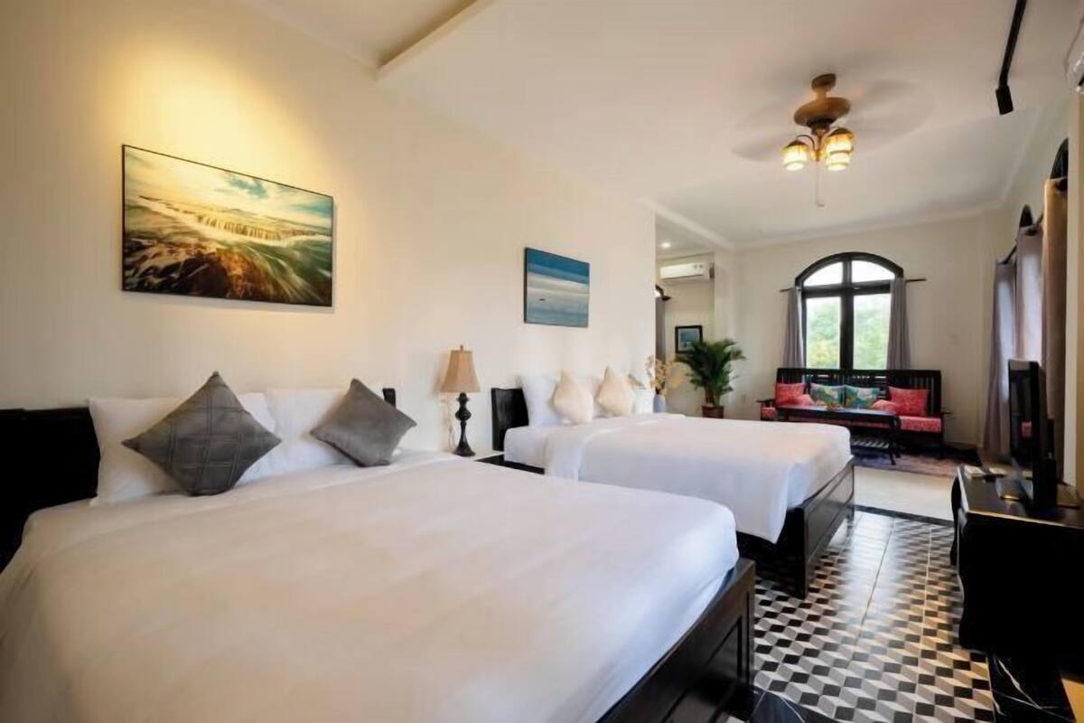 A hotel room with two beds, a checkered floor, a painting on the wall, and a desk with a chair.