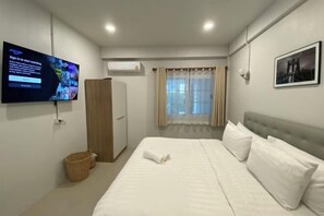 Habitación de hotel con cama, televisor, armario, ventana con cortinas y un cuadro en la pared.
