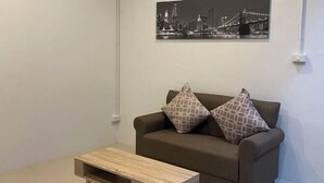 A modern living room with a brown sofa, patterned cushions, a small wooden coffee table, and a cityscape painting on the wall. - TWOHOME Near Nimman (Chiang Mai)