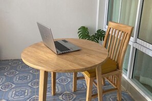 Een ronde houten tafel met een laptop erop, een houten stoel met een geel kussen en een vloer met een patroon.