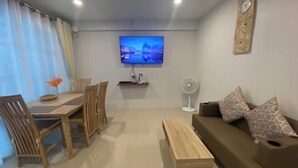 A living room with a wooden dining table, chairs, a sofa, a TV mounted on the wall, and a clock. - TWOHOME Near Nimman (Chiang Mai)