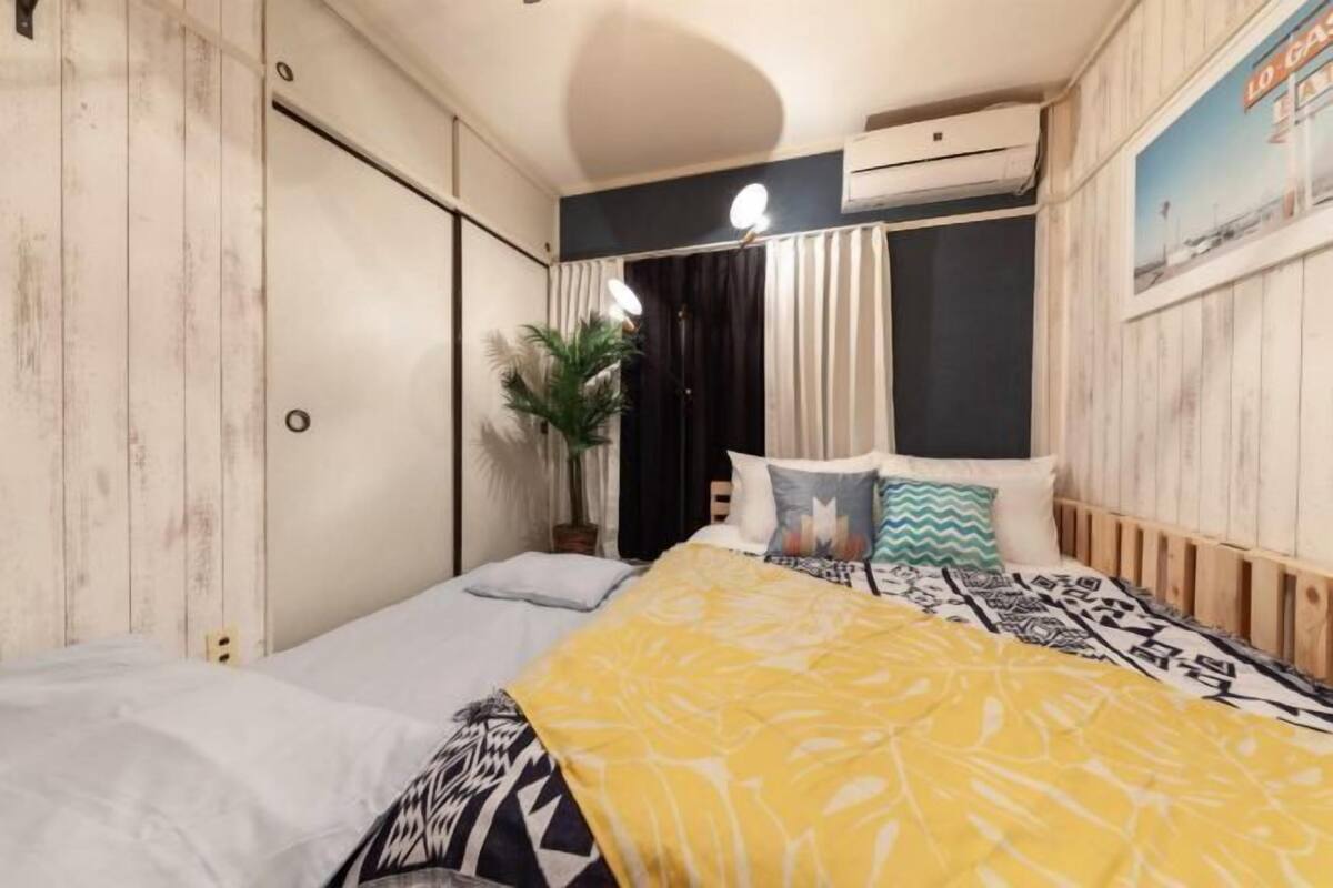 Une chambre à coucher avec un lit, une table de chevet, une plante en pot et un climatiseur fixé au mur.