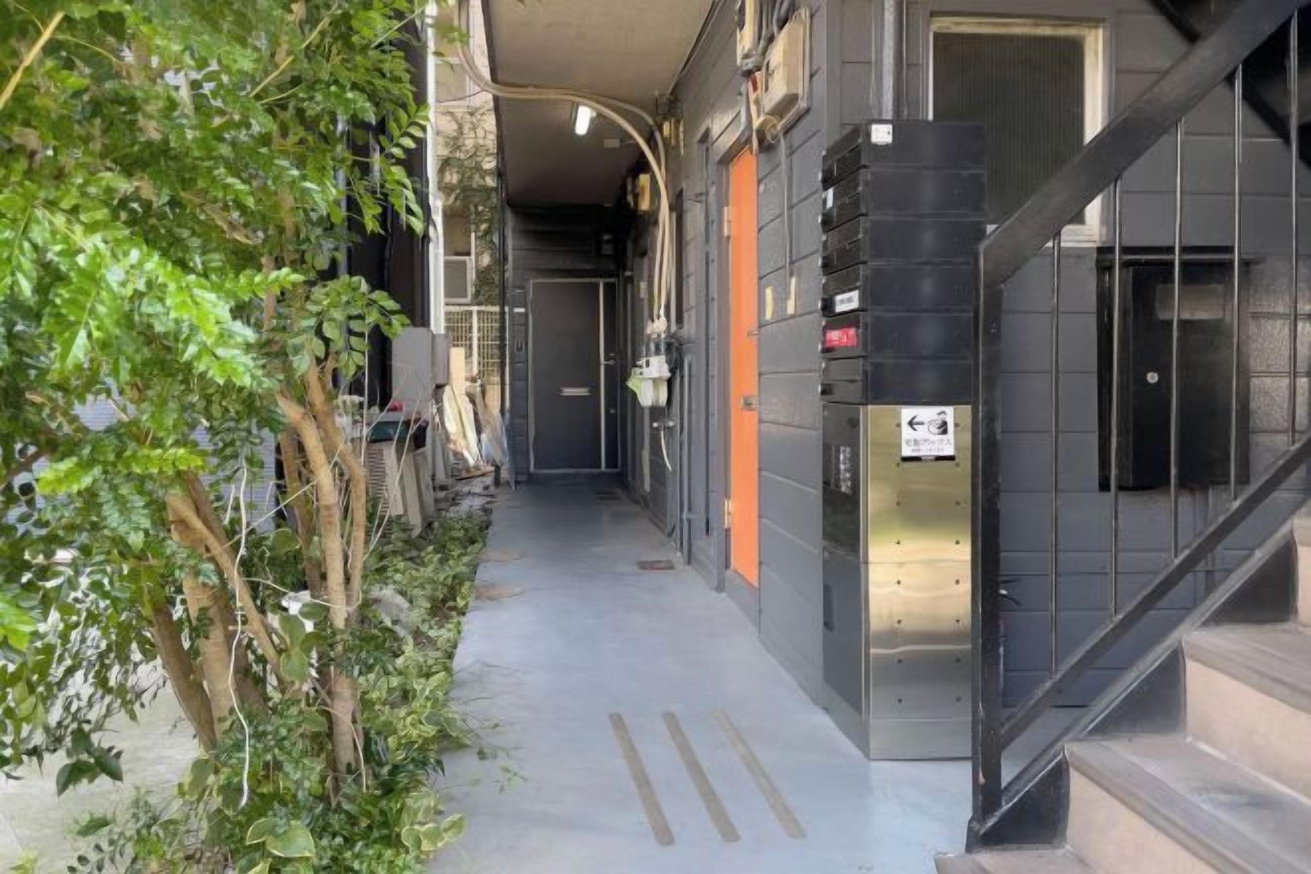 A narrow corridor with a staircase on the right, a door with a sign, and a small plant on the left.