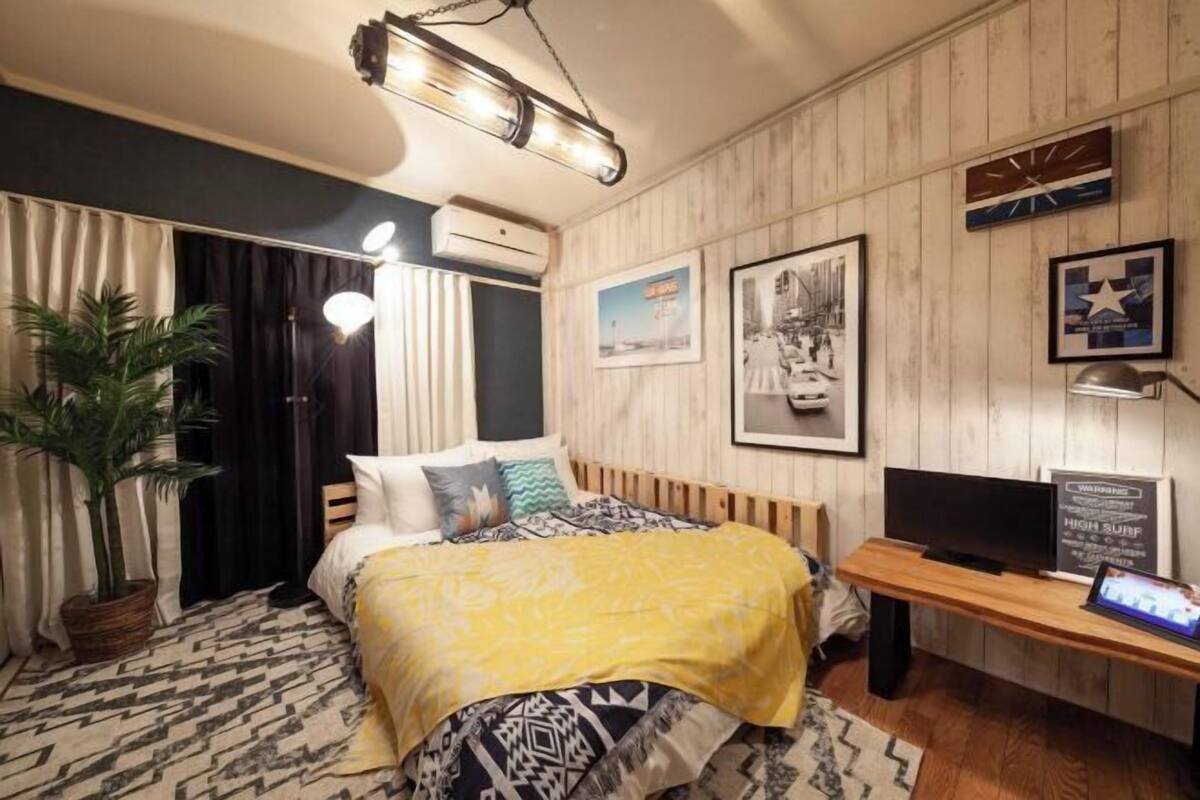 A bedroom with a bed, a desk, a television, and a potted plant.