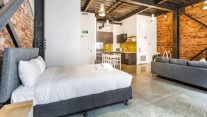 A modern hotel room with a bed, a sofa, a kitchenette, and a brick wall. - Modern Studio + Prime Location by Zodiak Stays (Auckland)