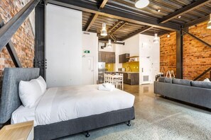 Une chambre d’hôtel moderne équipée d’un lit, d’un canapé, d’une kitchenette et d’un mur en briques.