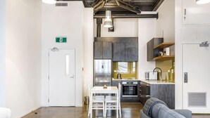 A modern kitchen with stainless steel appliances, a white door with an exit sign, and a gray sofa in a spacious area with a polished floor.