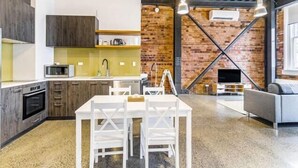 A modern kitchen with a brick wall, white cabinetry, and a dining area with a white table and chairs.