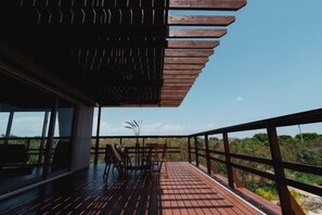 A wooden deck with a railing, a table, and chairs, overlooking a natural landscape.