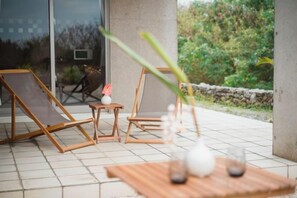 Un patio con dos sillones de madera, una mesita y un florero con flores.