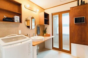 A modern bathroom with a built-in washing machine, a sink, a mirror, and a shower area.