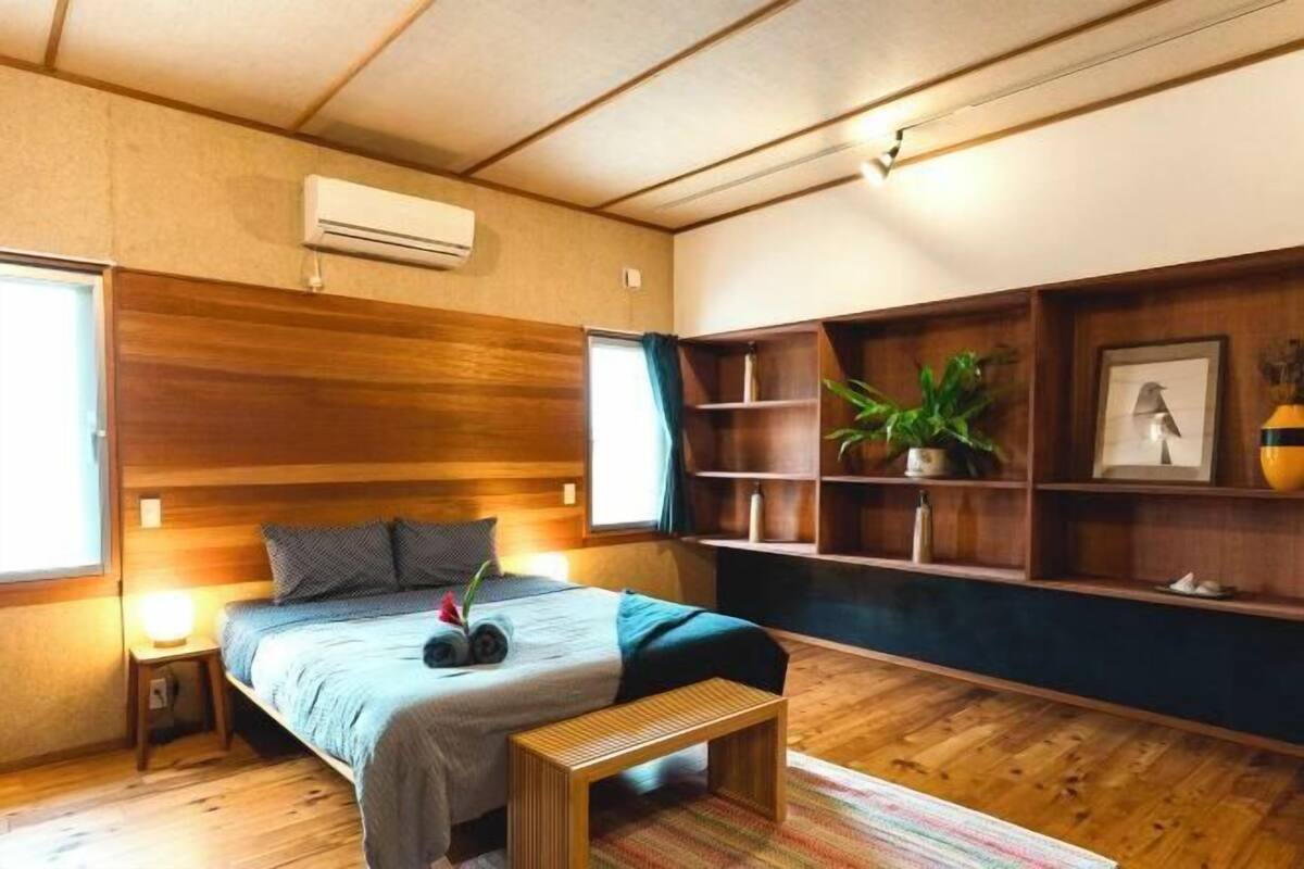 Une chambre à coucher comprenant un lit, des tables de chevet, un banc, une étagère avec des plantes et un appareil de climatisation.