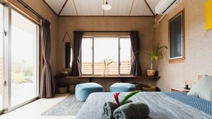 Een slaapkamer met een groot bed, een raam met gordijnen, een plant in pot en uitzicht op het buiten.