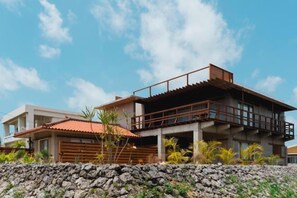Une maison moderne à deux étages, dotée d’un balcon, avec un mur de pierre en premier plan et un ciel dégagé.
