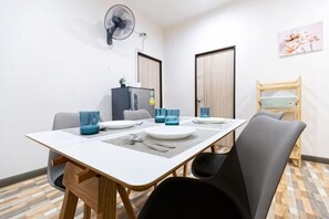 A dining area with a table set for four, chairs, a fan, a refrigerator, and a bunk bed in the background. - Summer Sea Villa Khanom (Khanom)