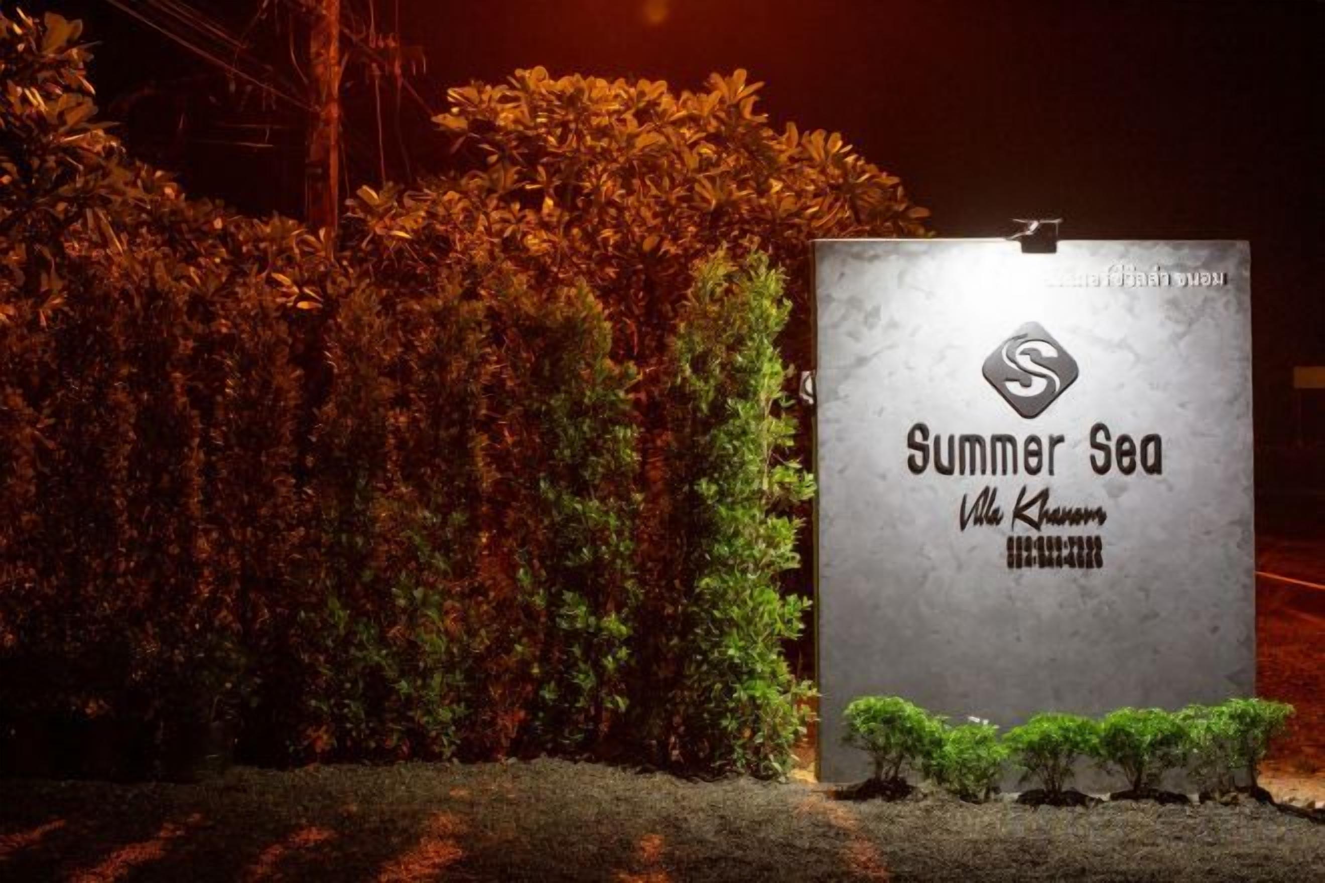 Cartell de 'Summer Sea Villa Khao Nam' amb un logotip, envoltat de tarrons i arbustos ben cuidats.