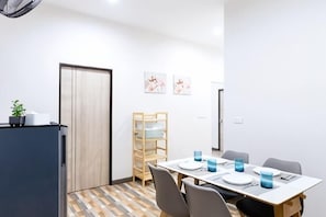 A dining area with a table set for four, chairs, a wooden chair, a small plant, and framed artwork on the wall. - Summer Sea Villa Khanom (Khanom)