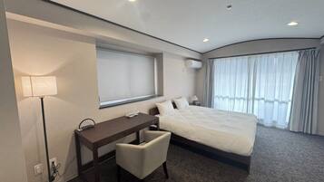 A modern hotel room with a large bed, a desk, a chair, a lamp, and a window with curtains.