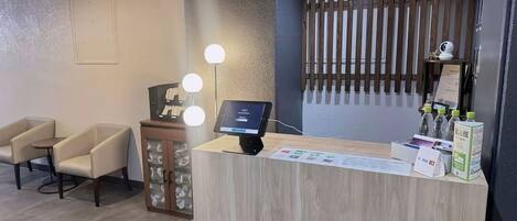 Un mostrador de recepción con una pantalla digital, una barra de madera y una zona de estar con dos sillas.