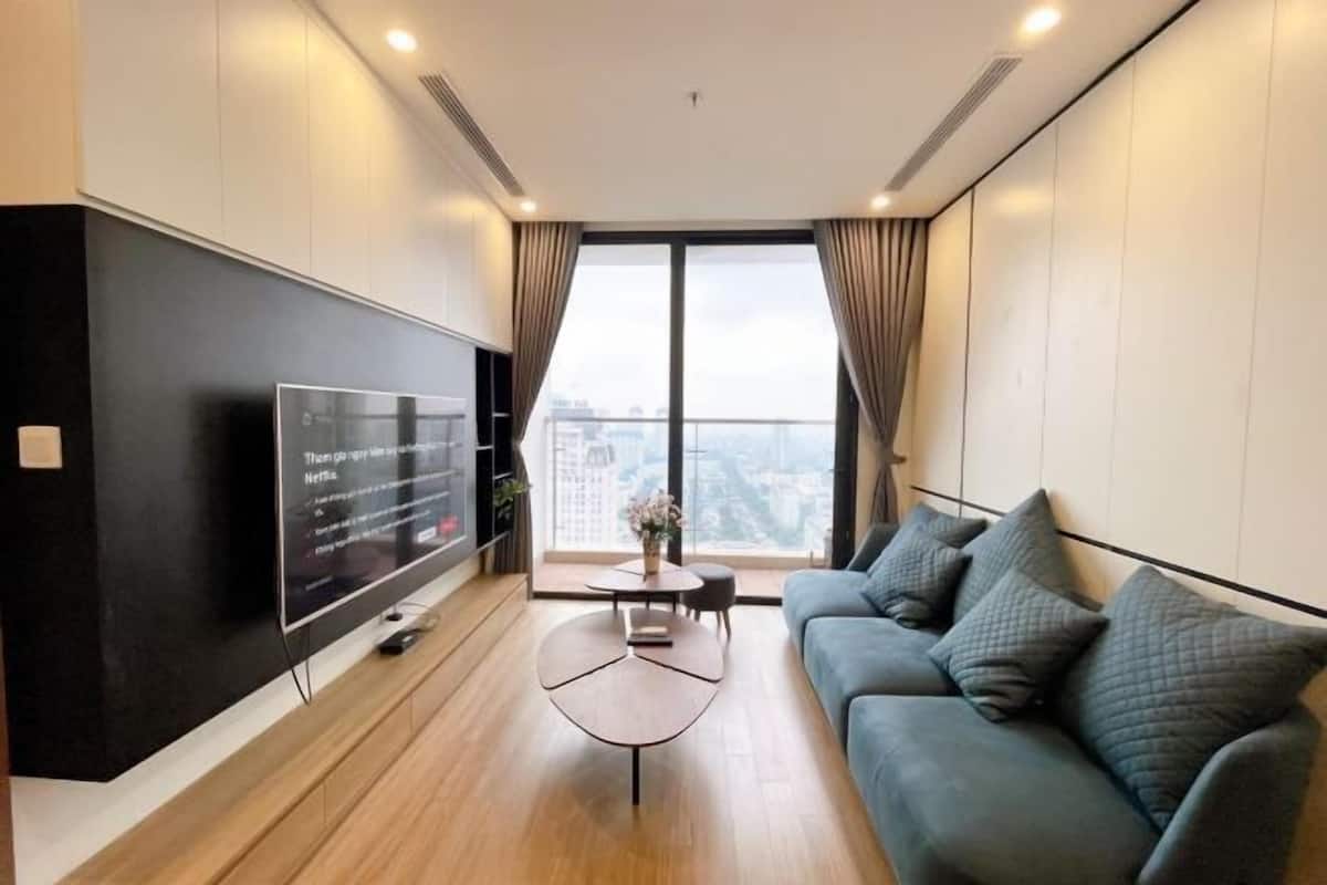 A modern living room with a flat-screen TV, a sofa, a coffee table, and a large window with curtains.