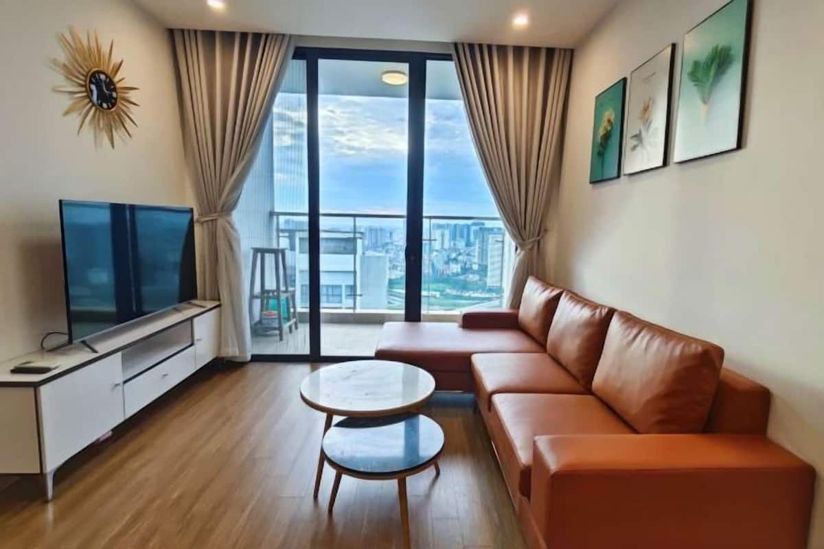 A modern living room with a large window, a leather sofa, a TV on a stand, and a small table.