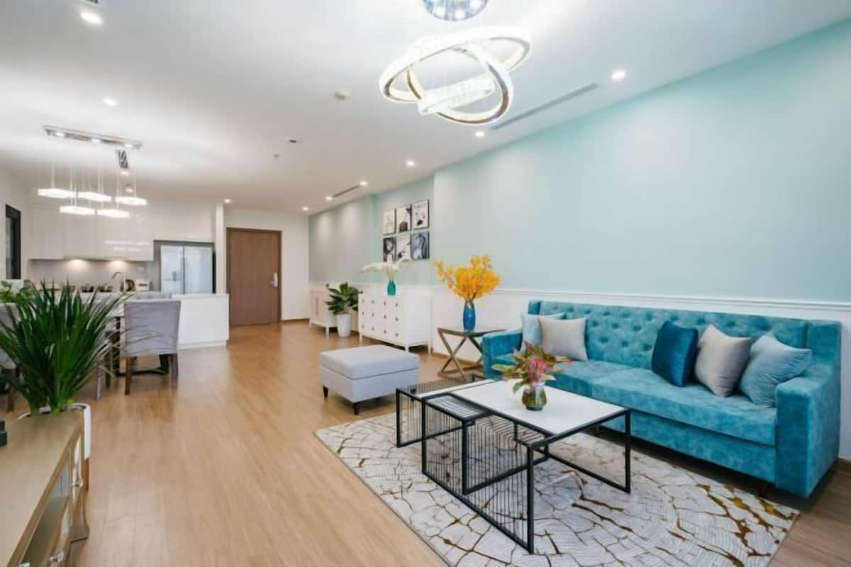 A modern living room with a blue sofa, a coffee table, and a dining area with a white table and chairs.