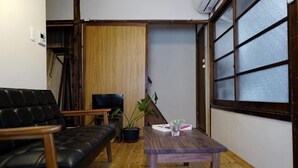 Una sala pequeña con un sofá, una mesa, una planta en maceta y un ventanal corredero.