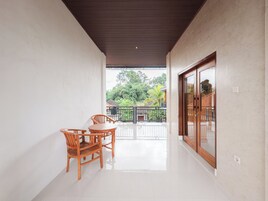 Um corredor com uma mesa e cadeiras de madeira, que leva a uma varanda com vista para vegetação e uma casa tradicional.