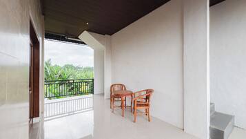 A spacious balcony with a wooden table and chairs, a view of greenery, and a white tiled floor.