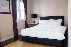 A neatly made bed with white bedding, a black headboard, and a small bedside table with a lamp. - Sol Stay Sukhumvit 16 Entire House Three Bedroom & Full Kitchen (Bangkok)