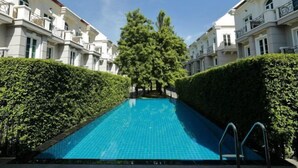 A swimming pool with a tiled surface, flanked by neatly trimmed hedges and white buildings with balconies. - Sol Stay Sukhumvit 16 Entire House Three Bedroom & Full Kitchen (Bangkok)
