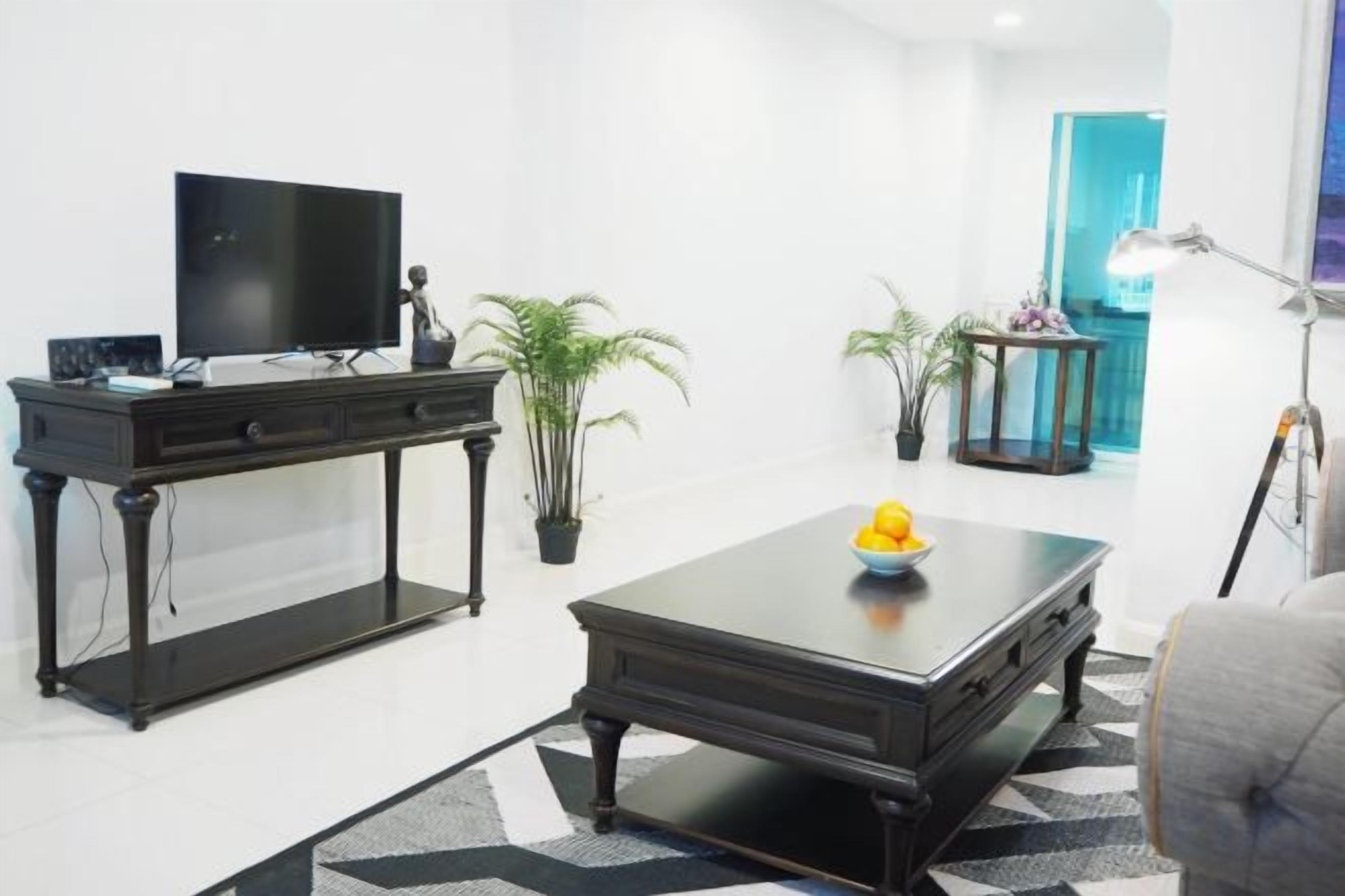 A modern living room with a flat-screen TV, a dark wooden coffee table, and two potted plants.