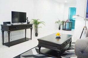 A modern living room with a flat-screen TV, a dark wooden coffee table, and two potted plants. - Sol Stay Sukhumvit 16 Entire House Three Bedroom & Full Kitchen (Bangkok)