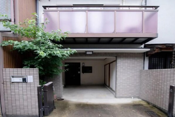 Un callejón estrecho con una reja, un pequeño árbol y la entrada a un edificio.