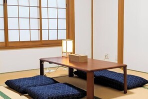 Um espaço com tatames, uma mesa de madeira baixa, dois almofadas e uma luminária.