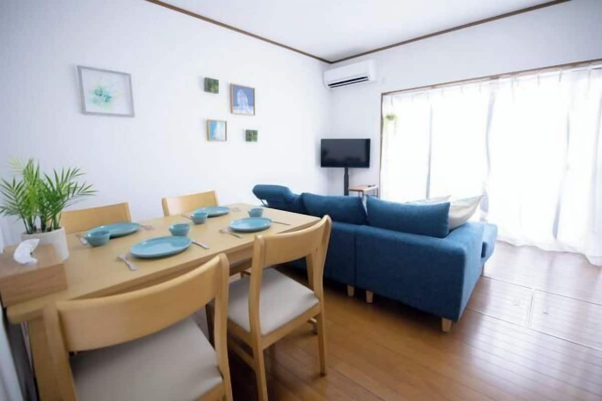 Un coin repas avec une table dressée pour quatre personnes, un canapé bleu, un téléviseur et une fenêtre avec des rideaux.