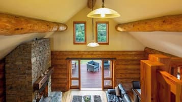 A log cabin interior with a stone fireplace, a leather sofa, and a view to an outdoor patio.