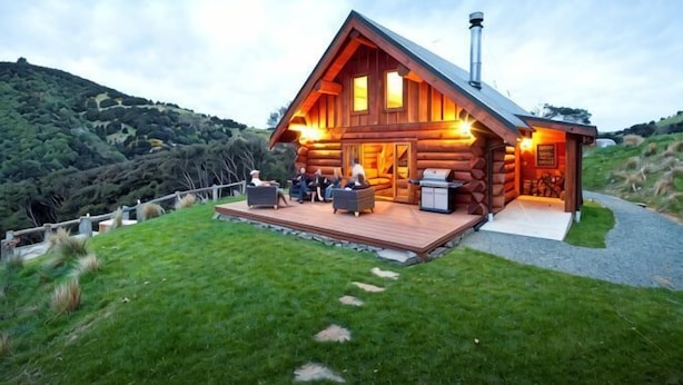 Una cabaña de troncos con terraza, chimenea y vistas del paisaje circundante.
