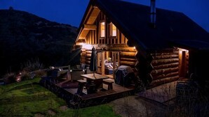 Una cabaña de troncos con un porche, asientos exteriores y una chimenea.