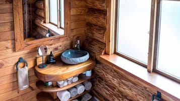 A wooden cabin-style bathroom with a stone sink, wooden shelves with towels, and a mirror.