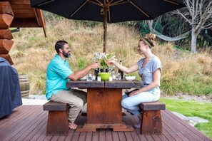 Two people seated at a wooden table with a black umbrella, surrounded by outdoor furniture on a wooden deck. - Cascade Creek Retreat (Circle Hill)