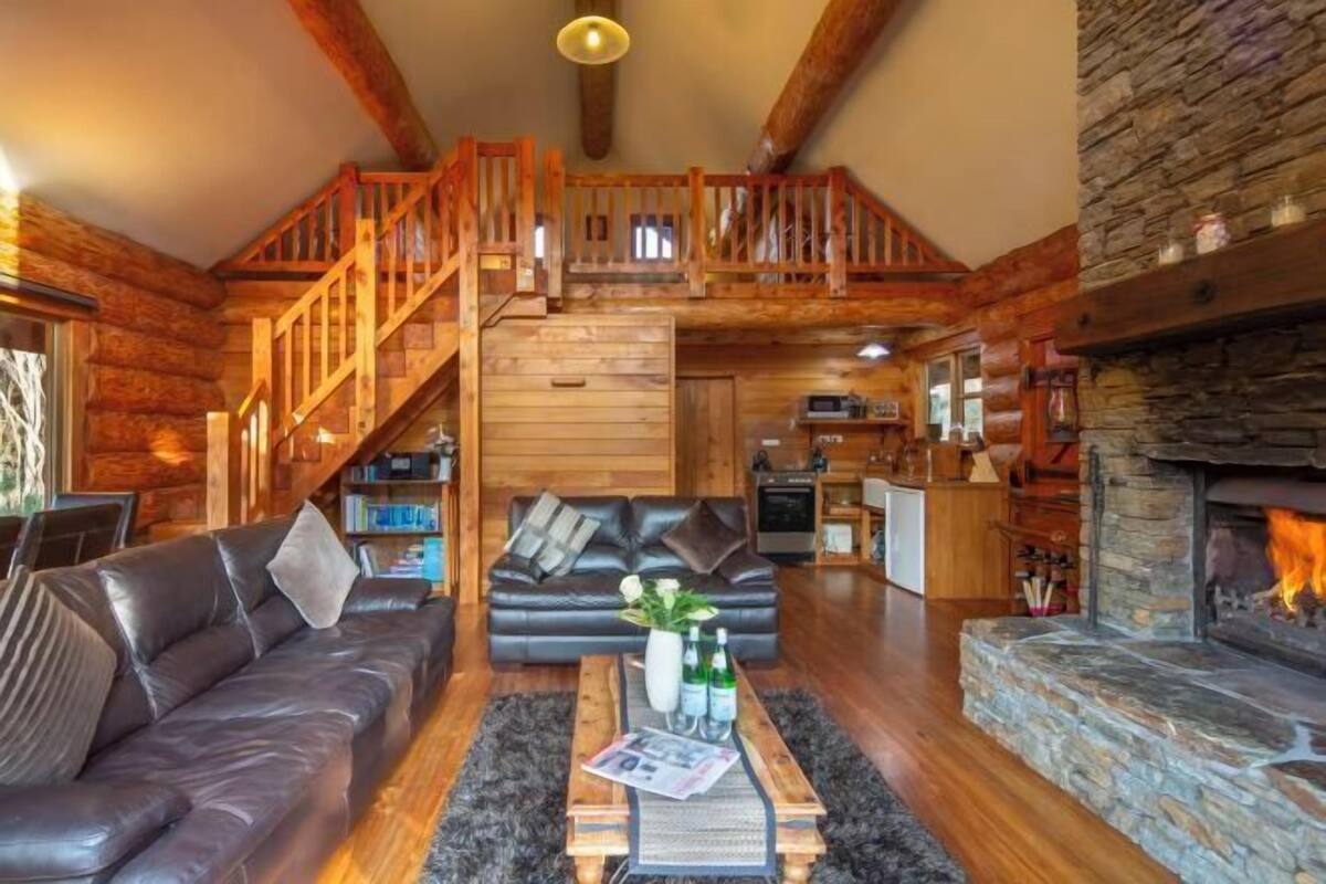 Ein rustikales Blockhaus-Interieur mit einer Holztreppe, Kamin, einer Couch und einem Essbereich.
