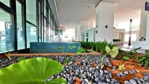 A modern hotel lobby with a large window, a seating area with a blue mosaic table, and a garden with plants and pebbles.