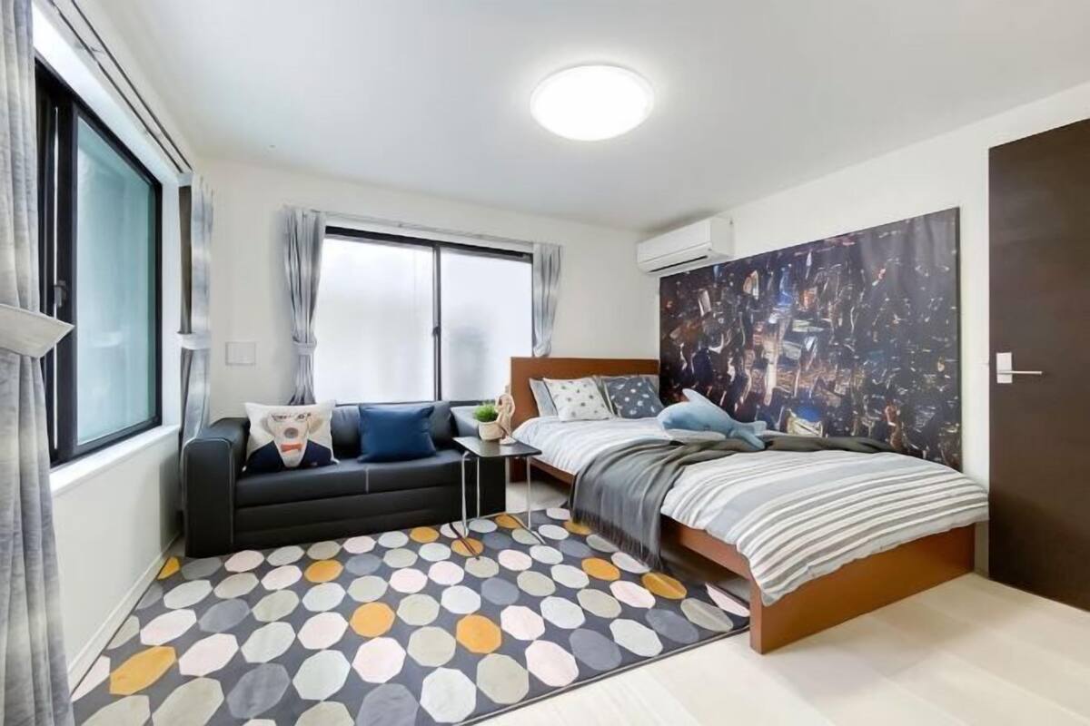 A bedroom with a bed, a sofa, a small table, and a large window.