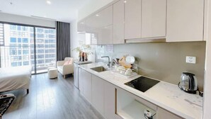 A modern kitchen with a sink, stove, and countertop. There is a dining area with a sofa and a window. - Yichen Apartment - Vinhomes Ocean Park Ha Noi (Hanoi)