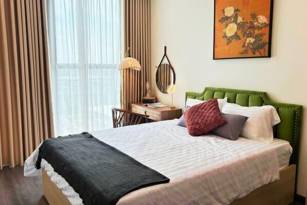 Uma cama bem arrumada com cabeceira verde, uma mesa com luminária e um quadro na parede.