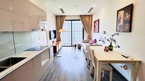 A modern kitchen with a built-in stove, a dining area with a table and chairs, and a large window with curtains. - Yichen Apartment - Vinhomes Ocean Park Ha Noi (Hanoi)